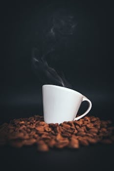 A steaming coffee cup surrounded by aromatic roasted coffee beans, perfect for coffee lovers.