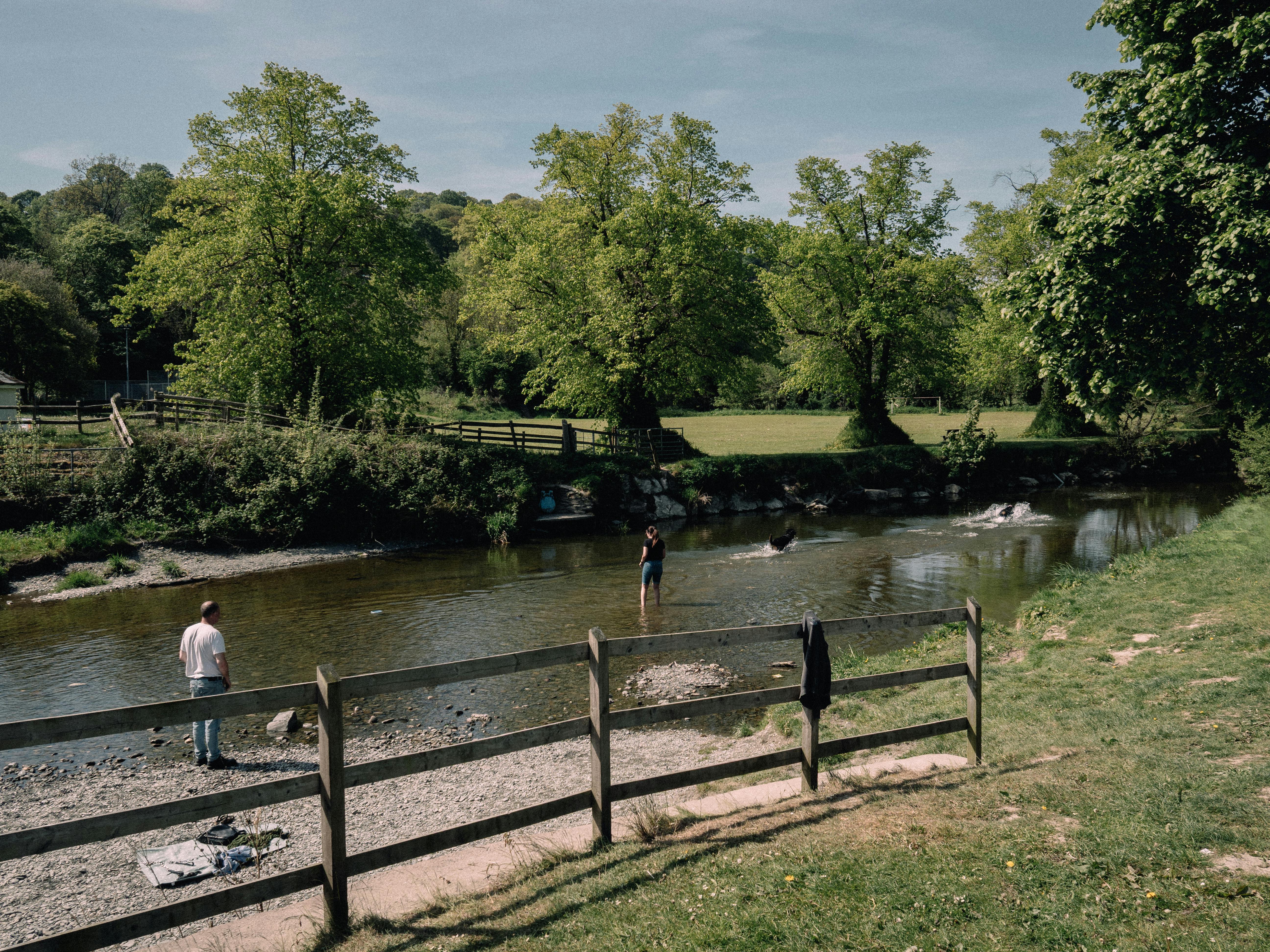 A tranquil summer scene at Llanfair Talhaiarn river with people enjoying the outdoors.