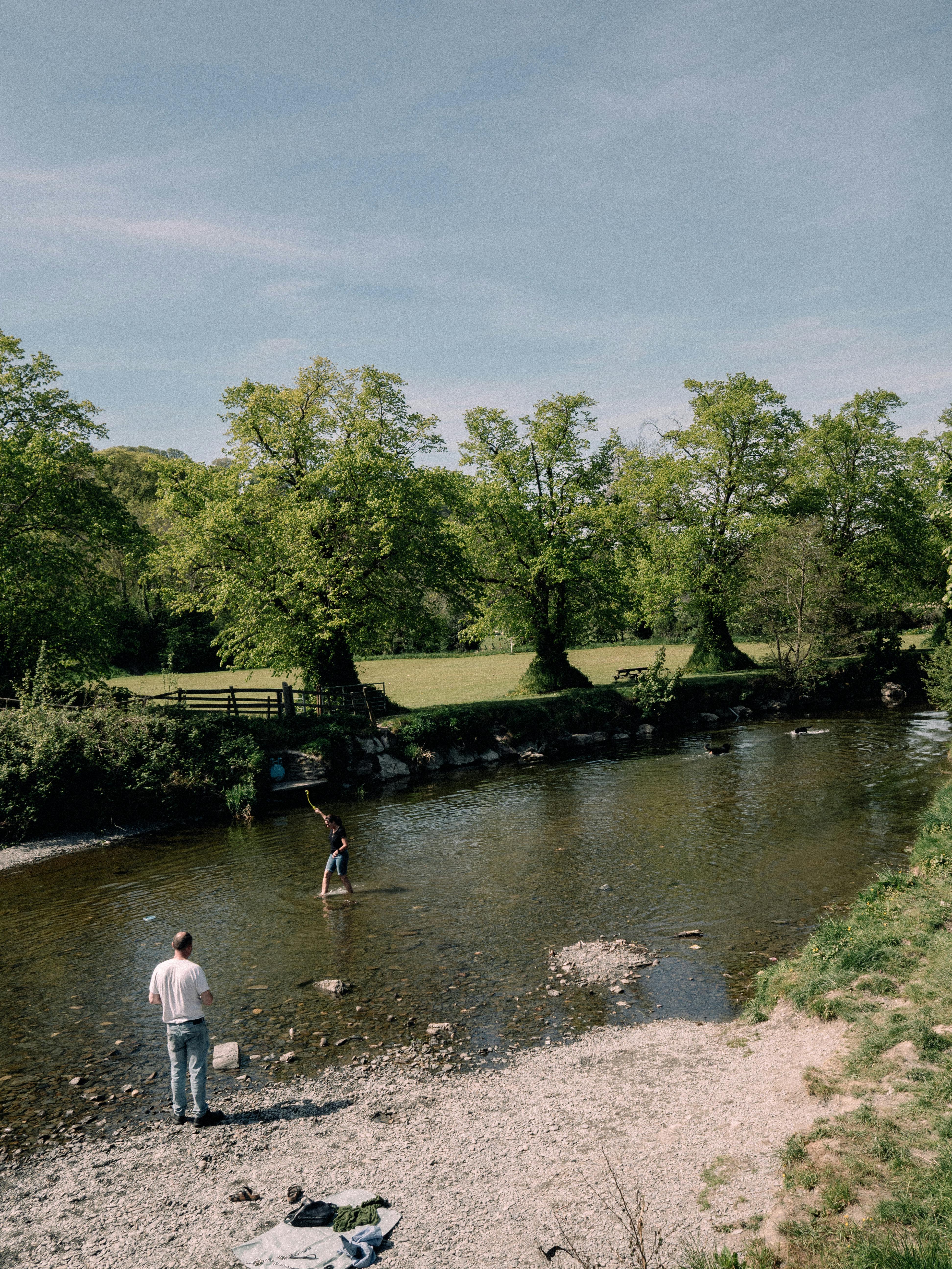 Two people enjoy the tranquility by a river in Llanfair Talhaiarn, Wales.