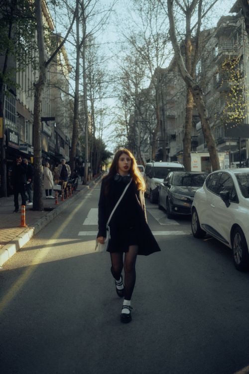 Free Confident young woman walking down a city street lined with trees and cars in the fall season. Stock Photo