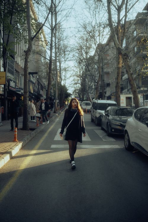Free Woman walking on a city street in the daytime with cars and buildings surrounding her. Stock Photo