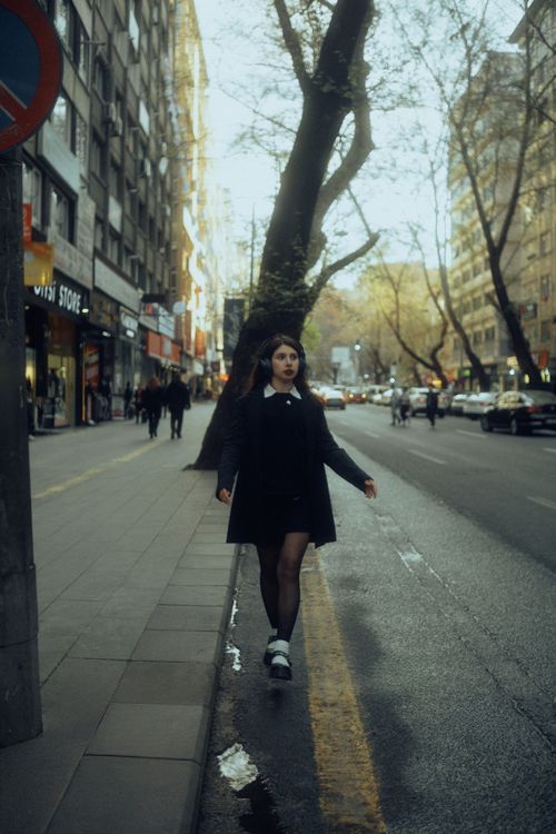 Free A woman in black coat walking along a bustling city street lined with trees and buildings. Stock Photo