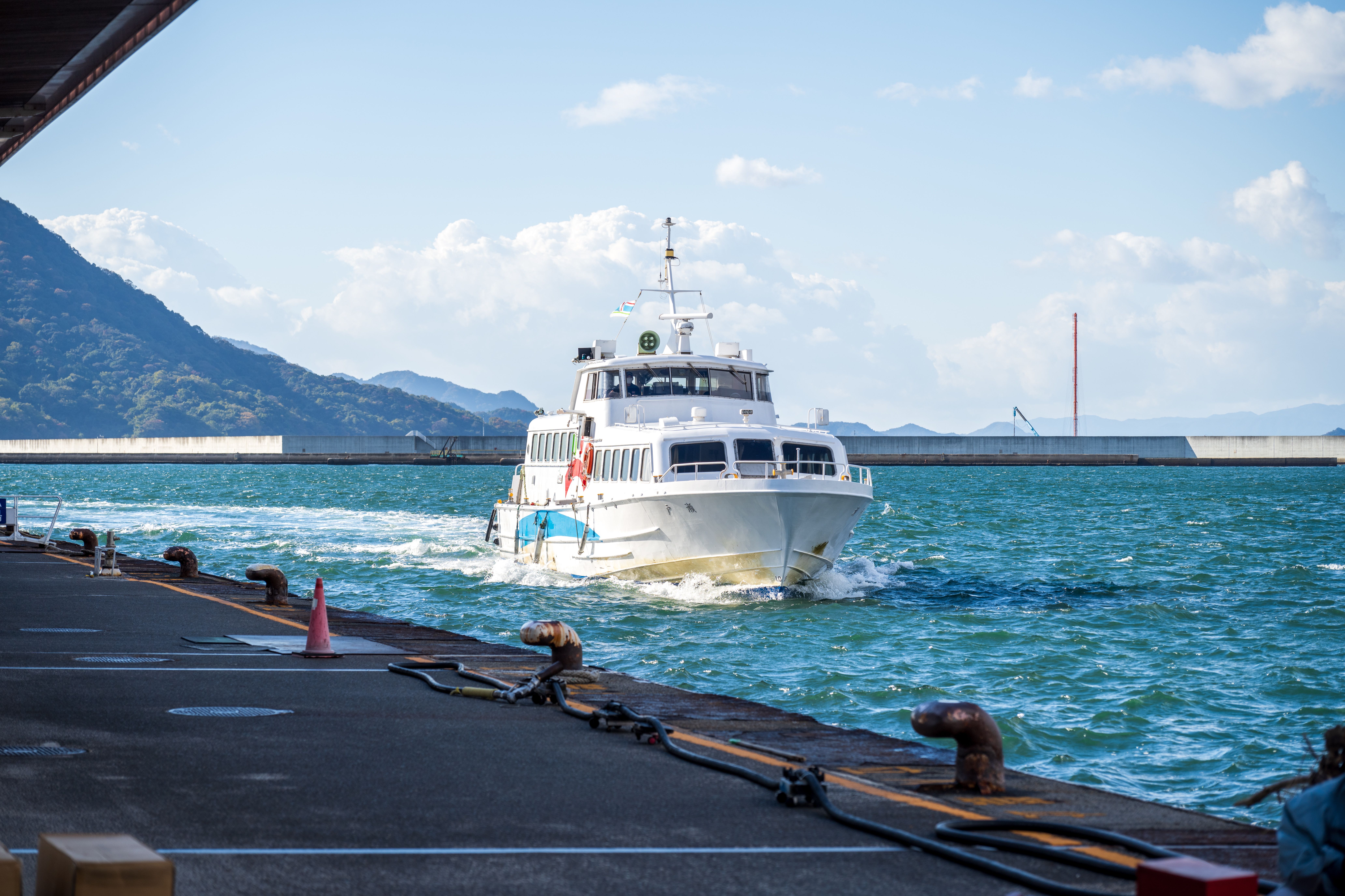 澄み切った空の下、山々を背景に鮮やかな青い海を背景に、白い旅客フェリーが港に近づいていきます。