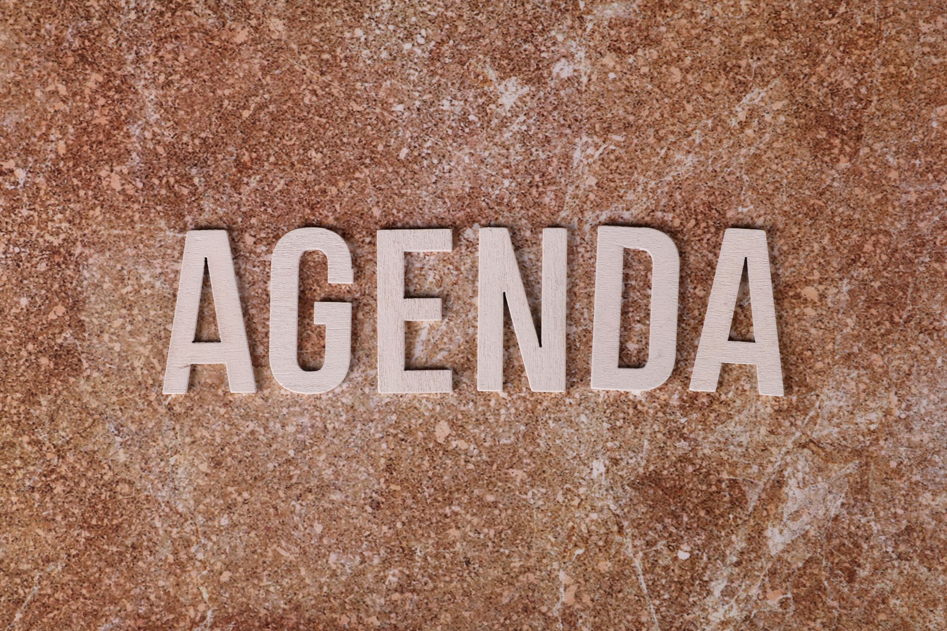 The word 'Agenda' spelled out with wooden letters on a textured brown surface.
