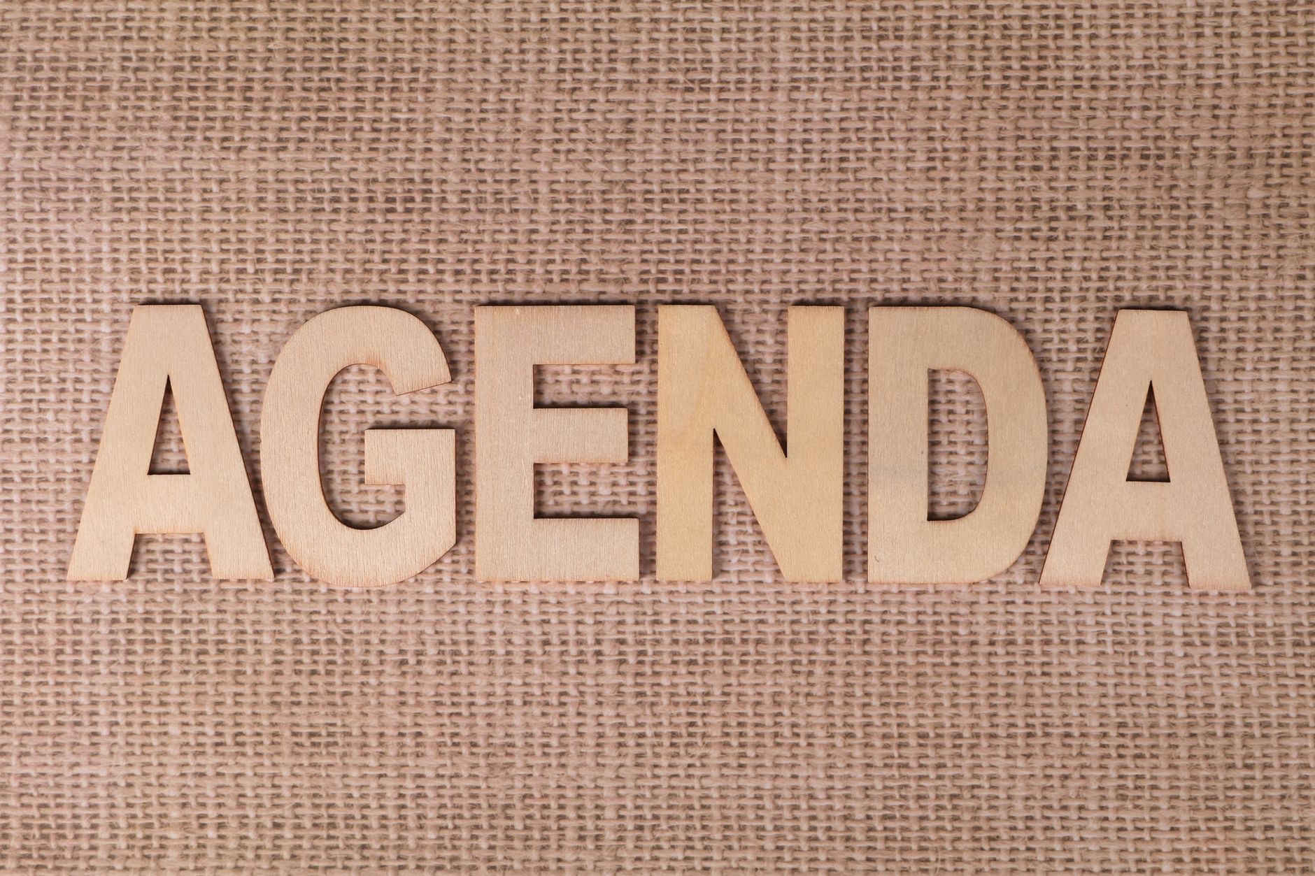 Wooden letters spelling 'AGENDA' on a textured burlap background.