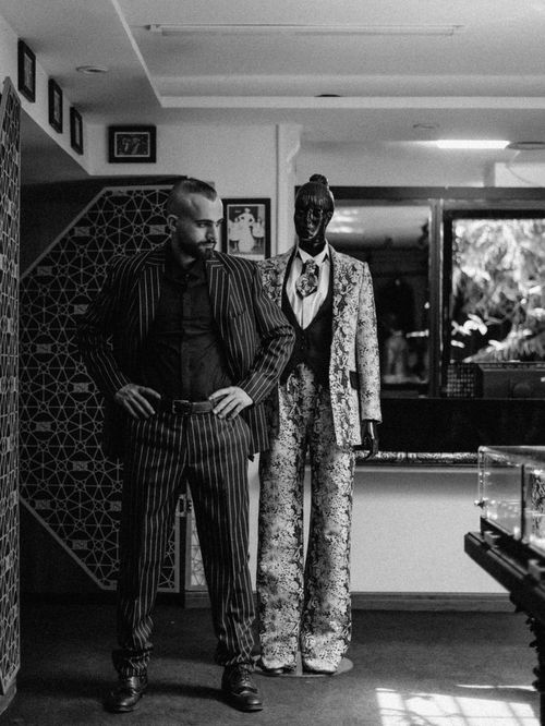 Free Black and white photo of a stylish man in a suit, posing indoors with a uniquely decorated mannequin. Stock Photo