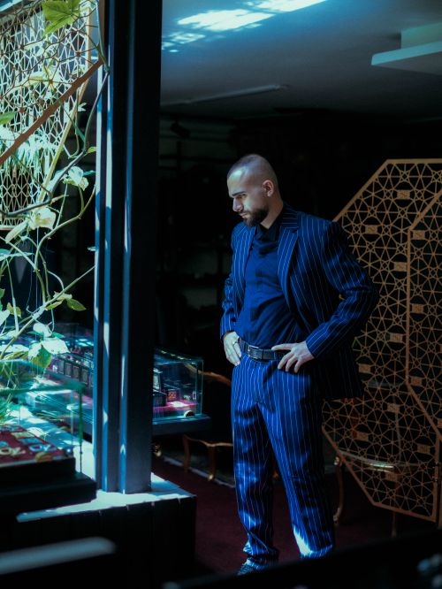Free A man in a blue pinstripe suit stands thoughtfully by a window in a stylish, modern interior. Stock Photo