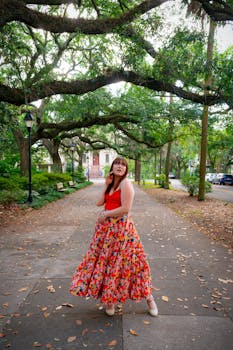 A fashionable woman posing in a vibrant outfit under lush trees in a Savannah park.