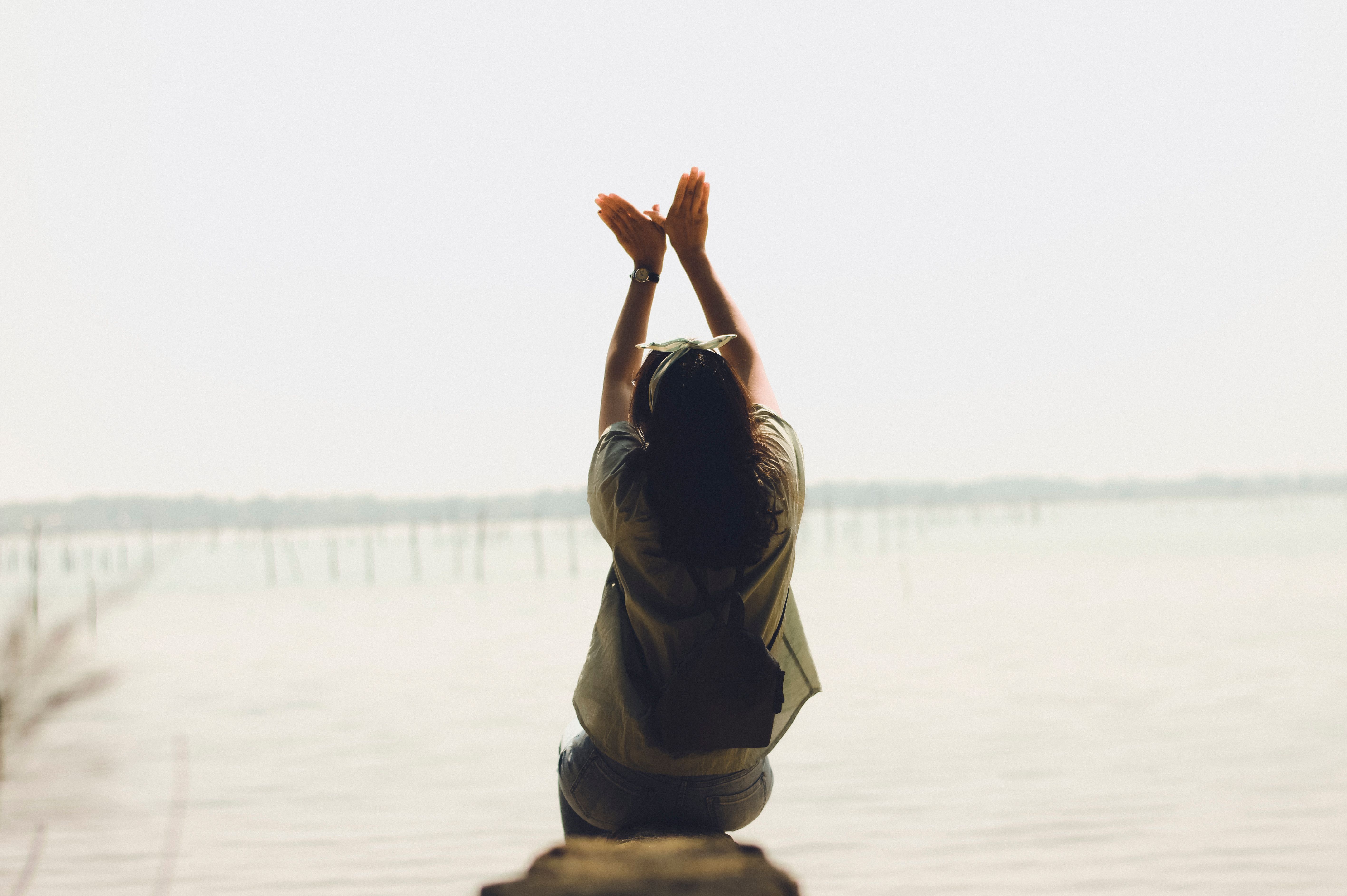 A serene moment of a woman raising her arms by a calm lake, embracing nature's tranquility.