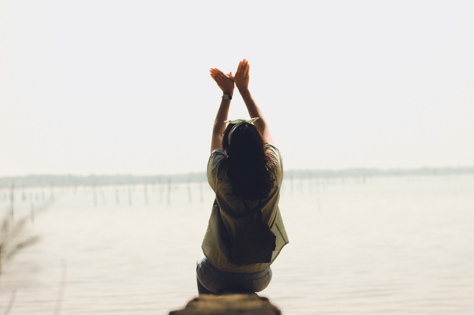A serene moment of a woman raising her arms by a calm lake, embracing nature's tranquility.