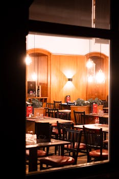 Warmly lit empty restaurant interior with wooden decor viewed through a window at night.