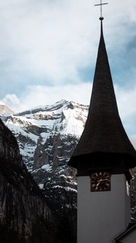 A church steeple stands against a majestic snowy mountain, showcasing alpine architecture.