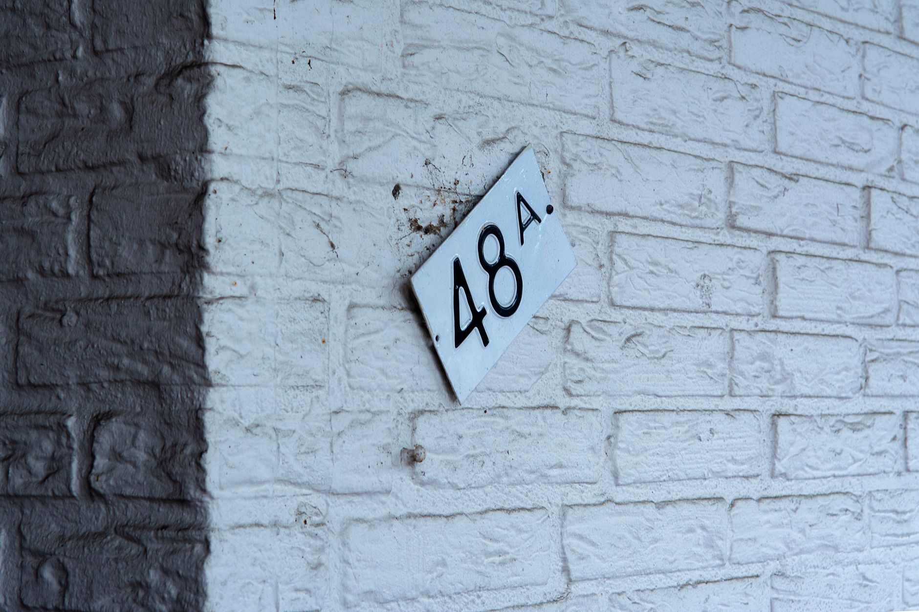 Close-up of a white brick wall featuring a tilted street number sign reading 48A.