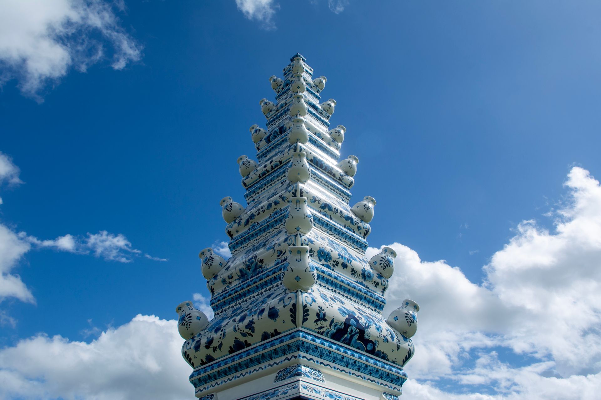 A porcelain Delft blue tower set against a vivid sky with clouds captures artistic elegance.