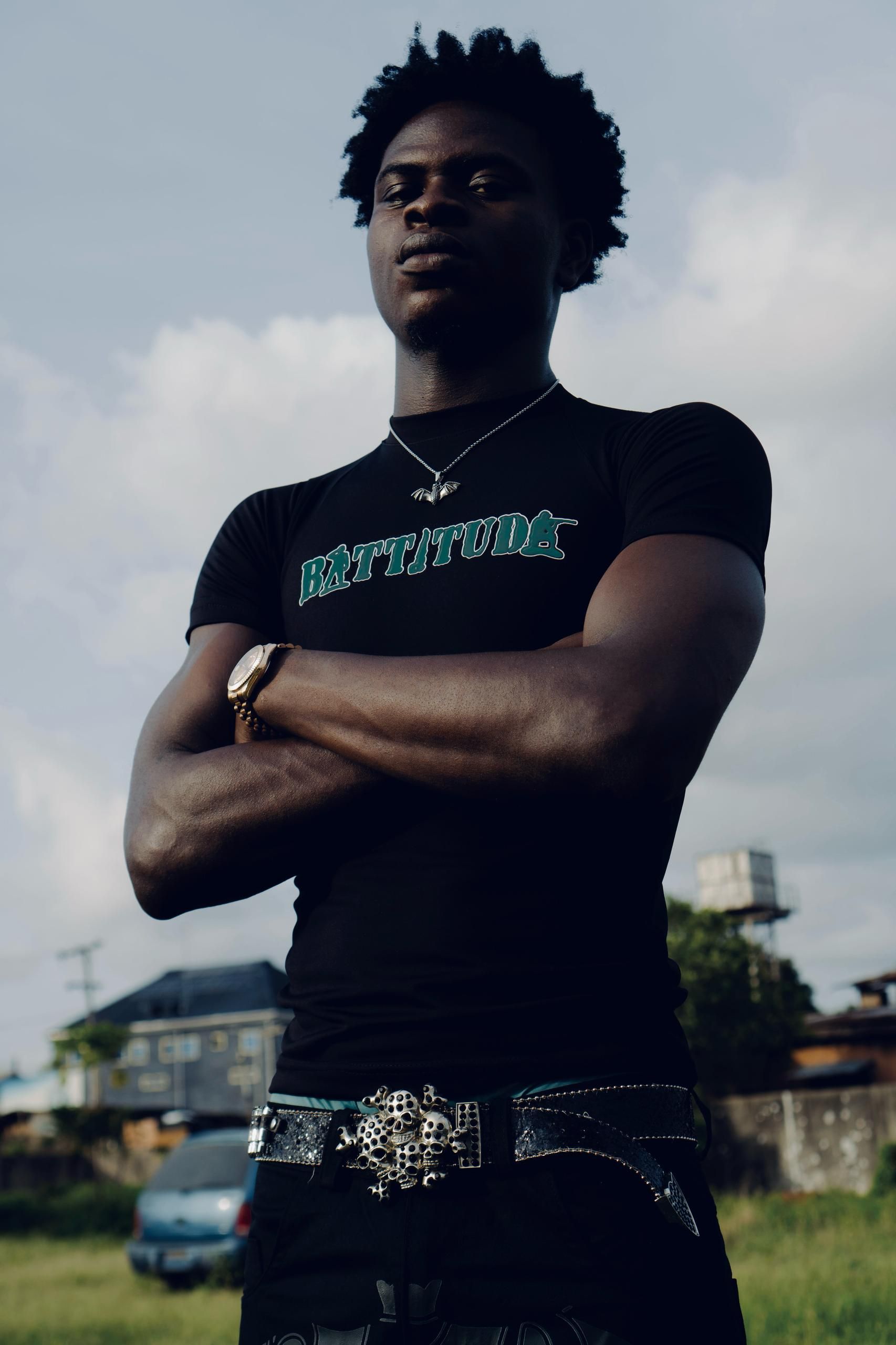 Portrait of a confident young man in fashionable black attire standing outdoors under a bright sky.