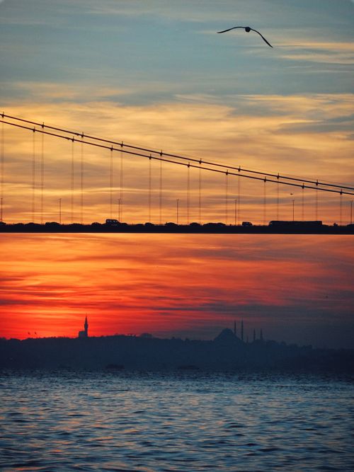 Free Dramatic sunset over a bridge with a colorful sky, silhouette of a city skyline, and tranquil waters. Stock Photo