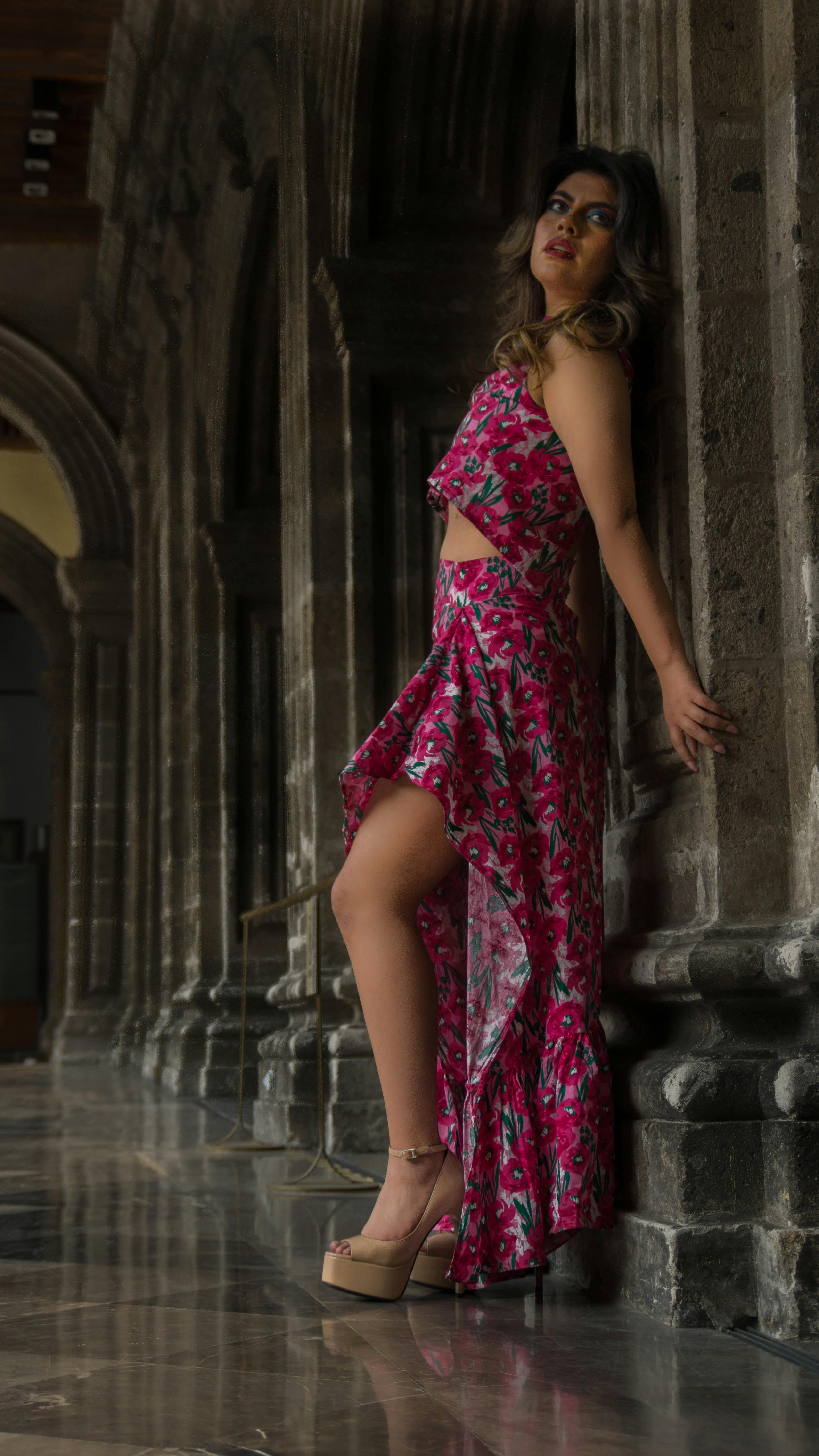Stylish woman in a bright floral dress poses elegantly against historical columns.