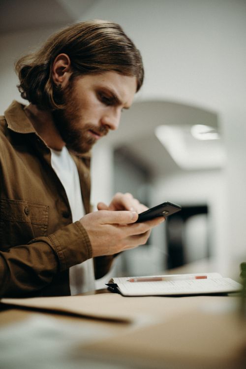 Free A concentrated man in an office environment intensely using his smartphone while sitting at a desk. Stock Photo