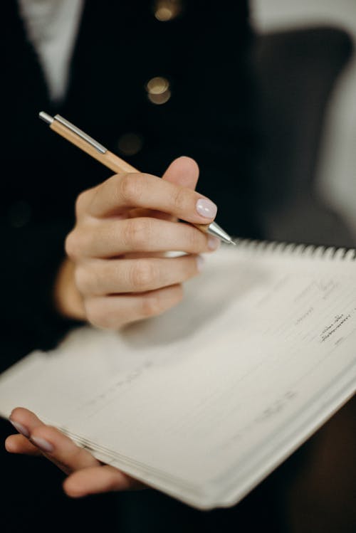 Persona Che Tiene La Penna Di Clic Arancione Scrivendo Sul Taccuino