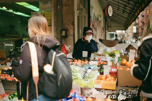A bustling outdoor market with colorful fruits and masked shoppers.