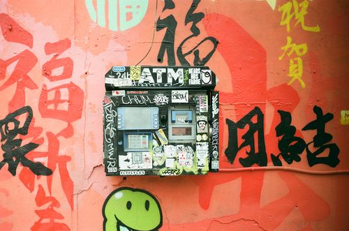 Free Street ATM covered in stickers and graffiti on a colorful urban wall. Stock Photo