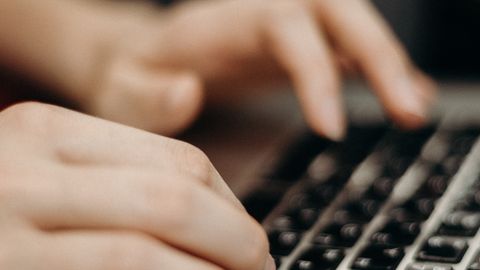 Close-up shot of hands typing on a laptop keyboard in a work environment.