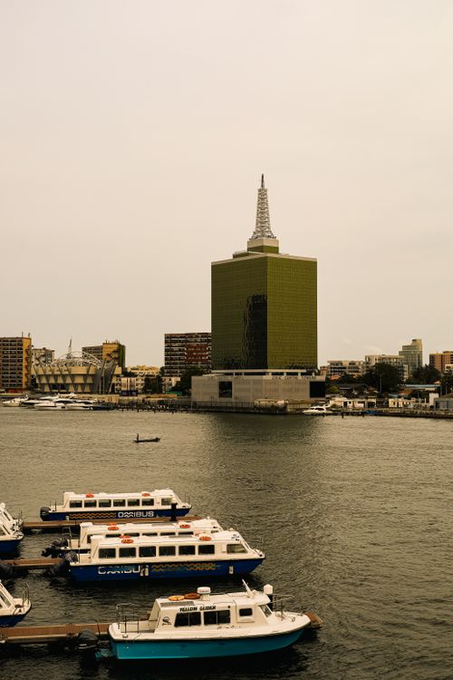 Free A serene view of Lagos waterfront with anchored boats and a notable skyscraper on a cloudy day. Stock Photo
