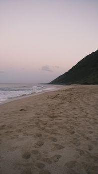 Peaceful sandy beach with gentle waves and a mountain, perfect for relaxation at sunrise.