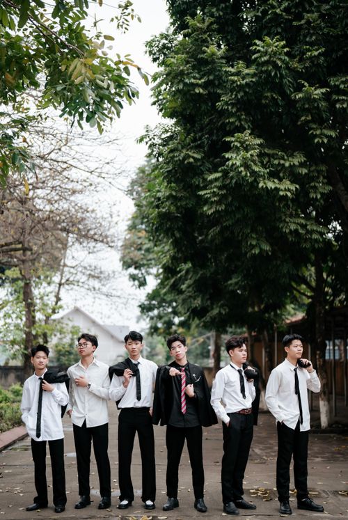 Free A group of six young men dressed in formal suits standing outdoors under trees. Stock Photo