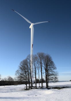 Wind turbine stands tall amidst snowy landscape under clear blue sky, showcasing renewable energy.