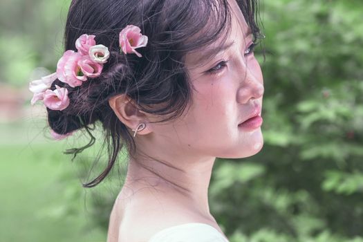 Elegant woman with floral hairpiece, peaceful expression, outdoors.