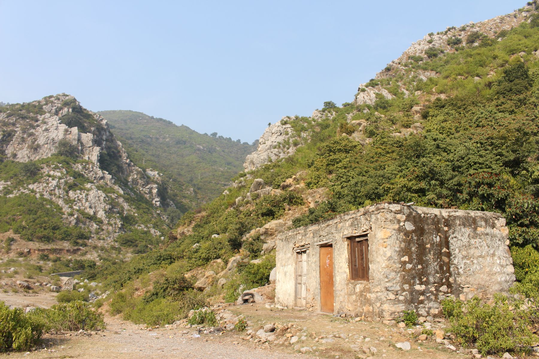 Rustic stone house amidst the lush Margalla Hills in Pakistan under blue sky.