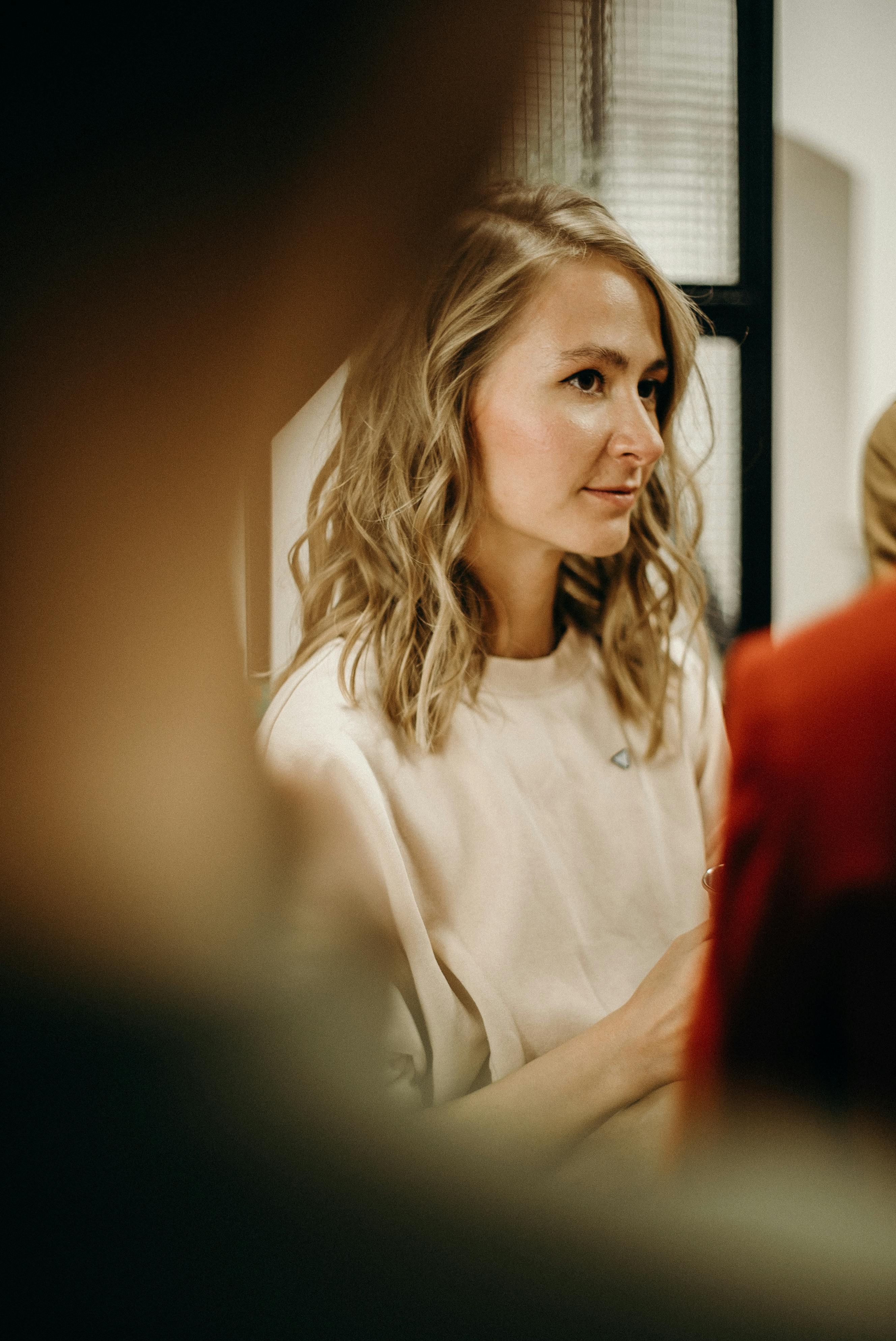 Portrait of a woman with blond hair indoors, surrounded by soft light and warm tones.