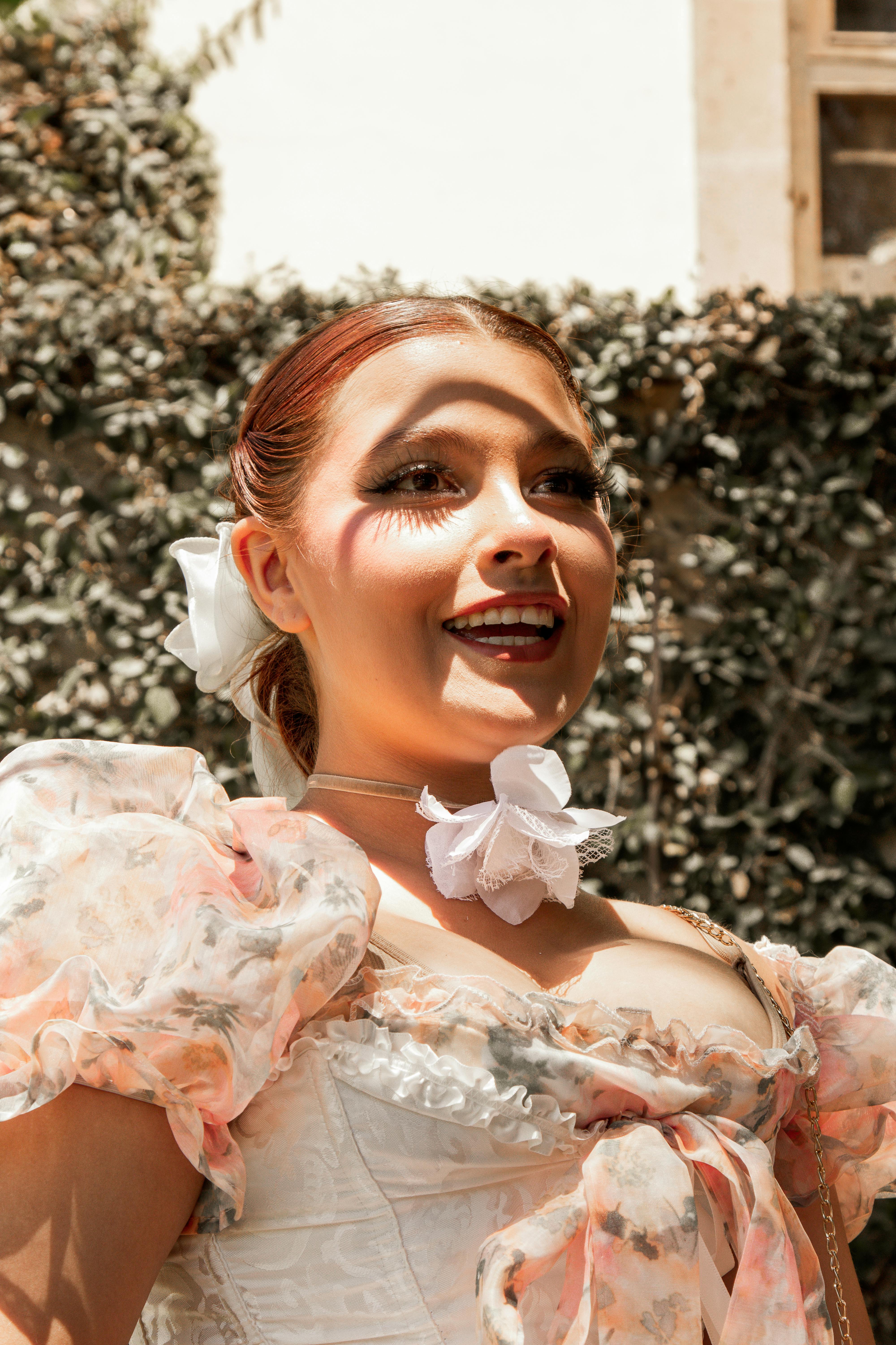 Free Smiling woman in vintage-style attire with floral accents and dramatic makeup outdoors. Stock Photo
