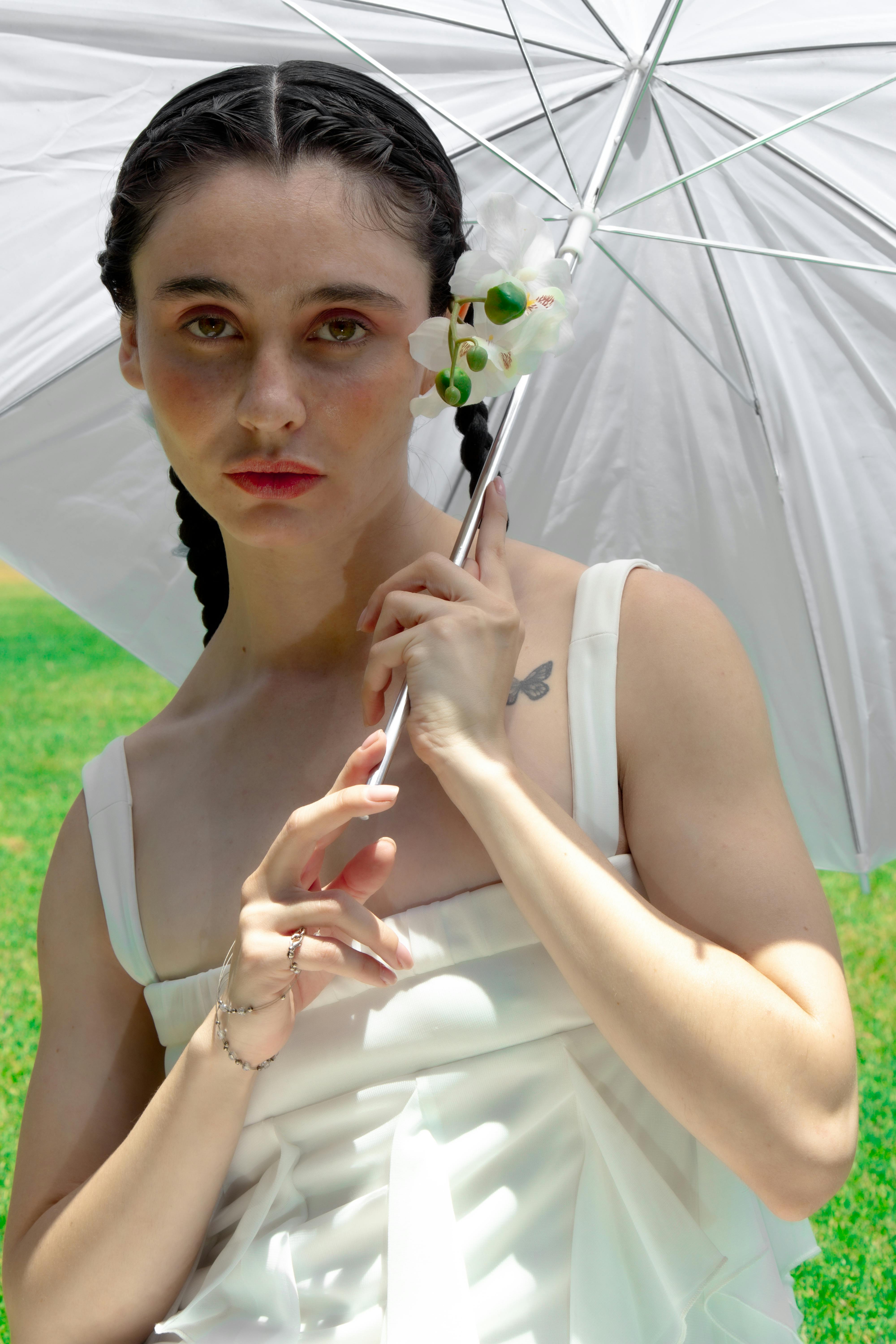 Portrait of a woman in a white dress holding a parasol in a green field, exuding elegance.