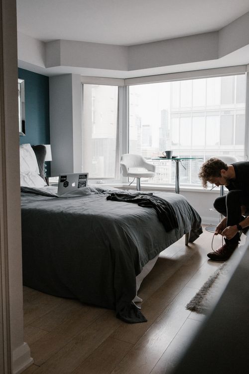 Free A person tying shoes in a well-designed city apartment with laptop and window view. Stock Photo