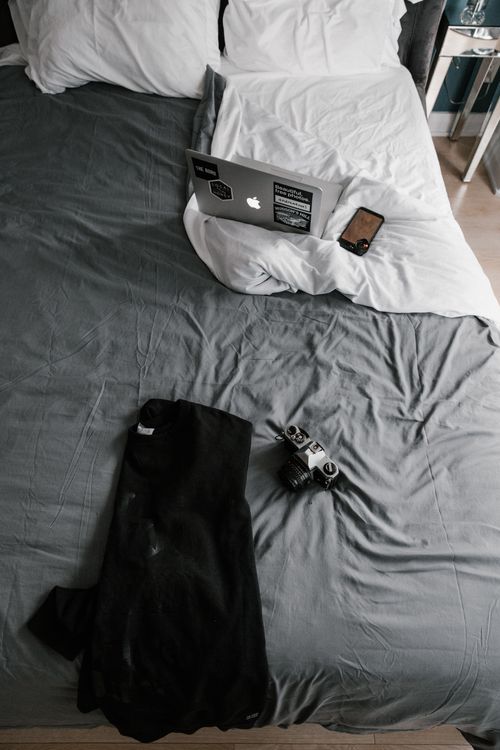 Free A comfortable bed with a laptop, smartphone, and vintage camera, ideal for remote work setups. Stock Photo
