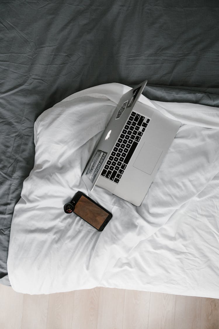 Silver Macbook Pro On White Bed Blanket