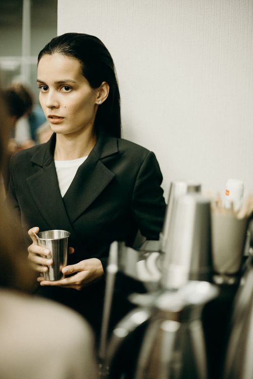Free Businesswoman in an office holding a drink, looking thoughtful. Indoors setting. Stock Photo