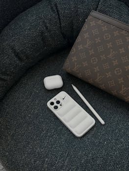 Stylish composition of luxury tech items and designer bag on a modern cushion, showcasing elegance and technology.