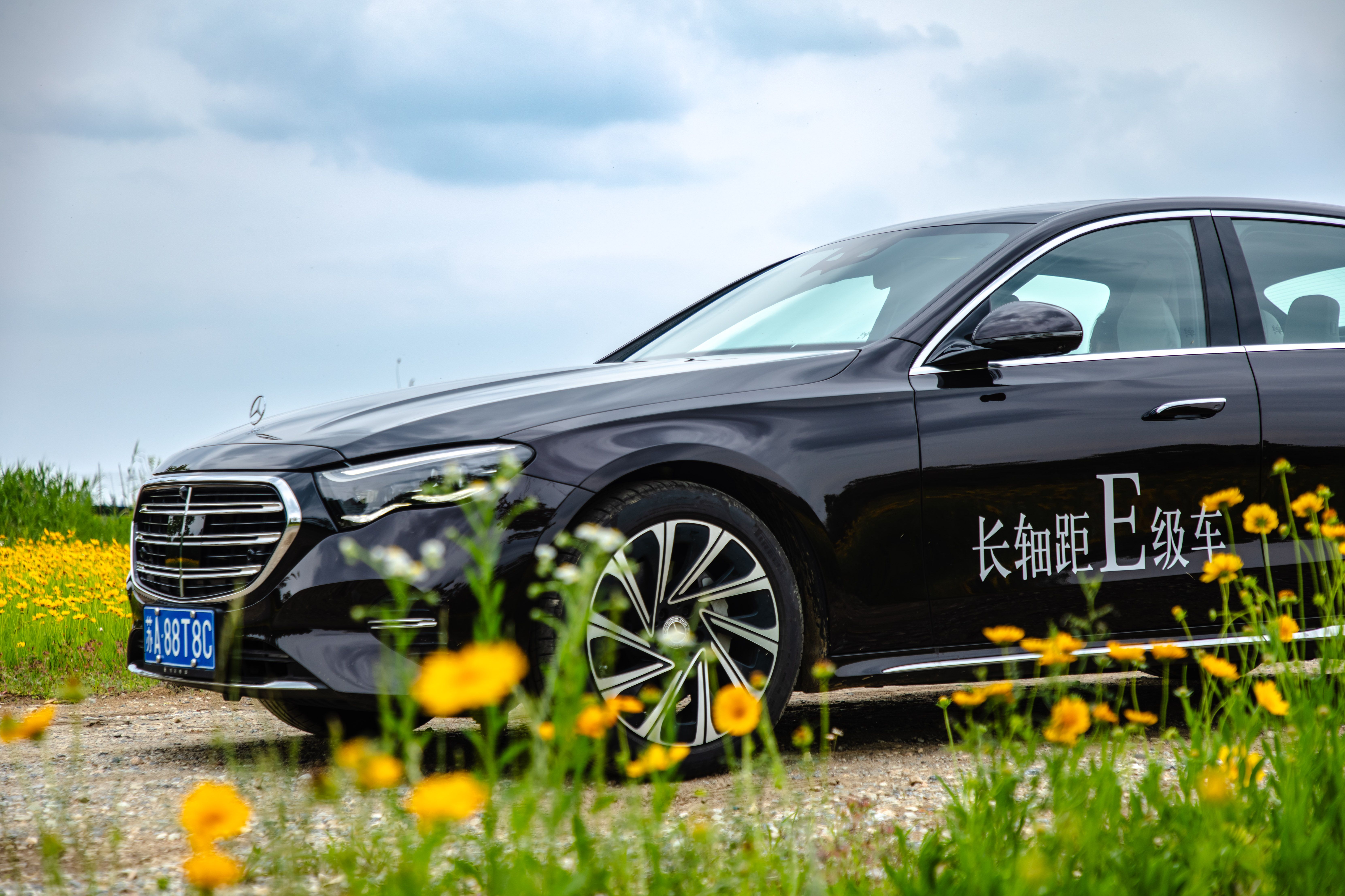 Black luxury sedan parked among yellow wildflowers under a cloudy sky