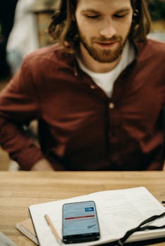 年轻人在咖啡馆里，拿着笔记本和笔坐在那儿玩手机