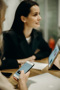 Two women in a meeting using smartphones and tablets in an office setting.