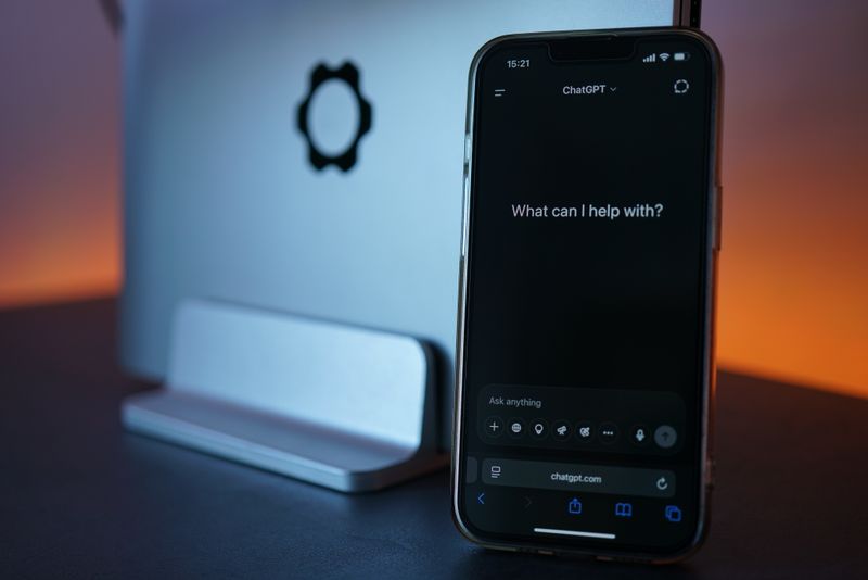 Close-up of a smartphone showing a chat interface with a laptop in the background