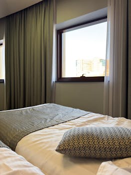 Modern hotel room with bed and cityscape view through window.