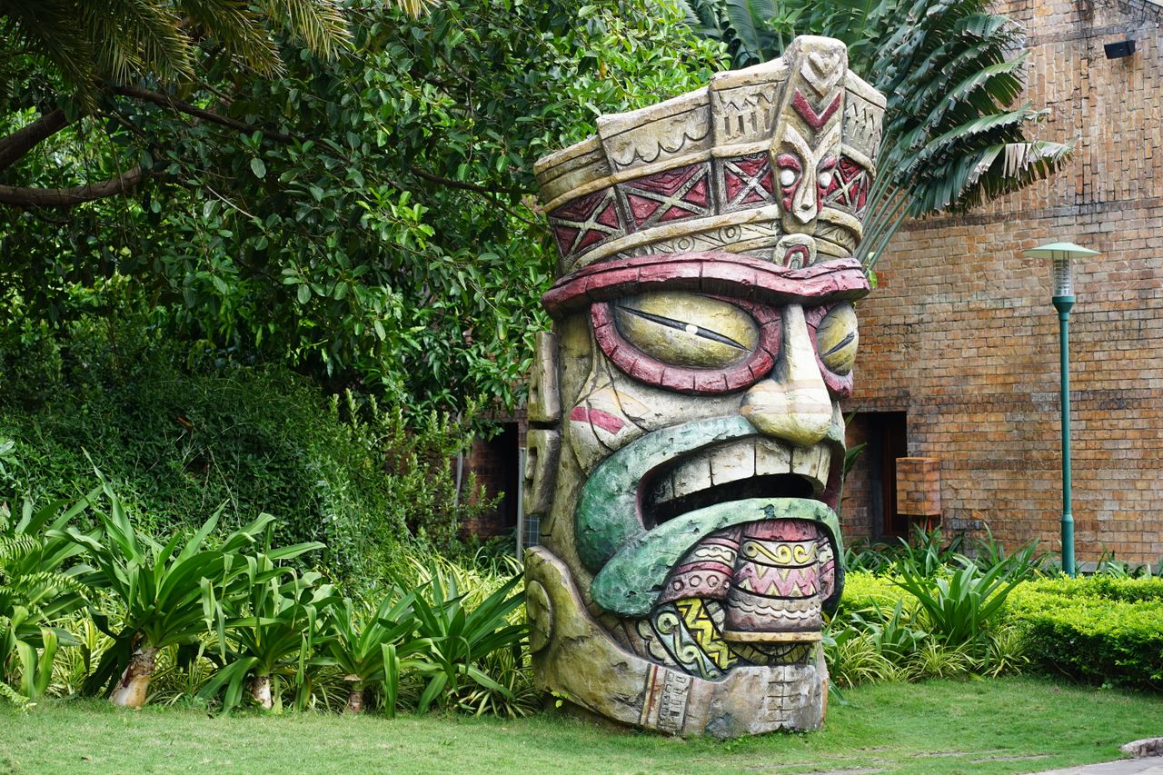 vibrant totem pole sculpture amidst greenery and brick wall backdrop
