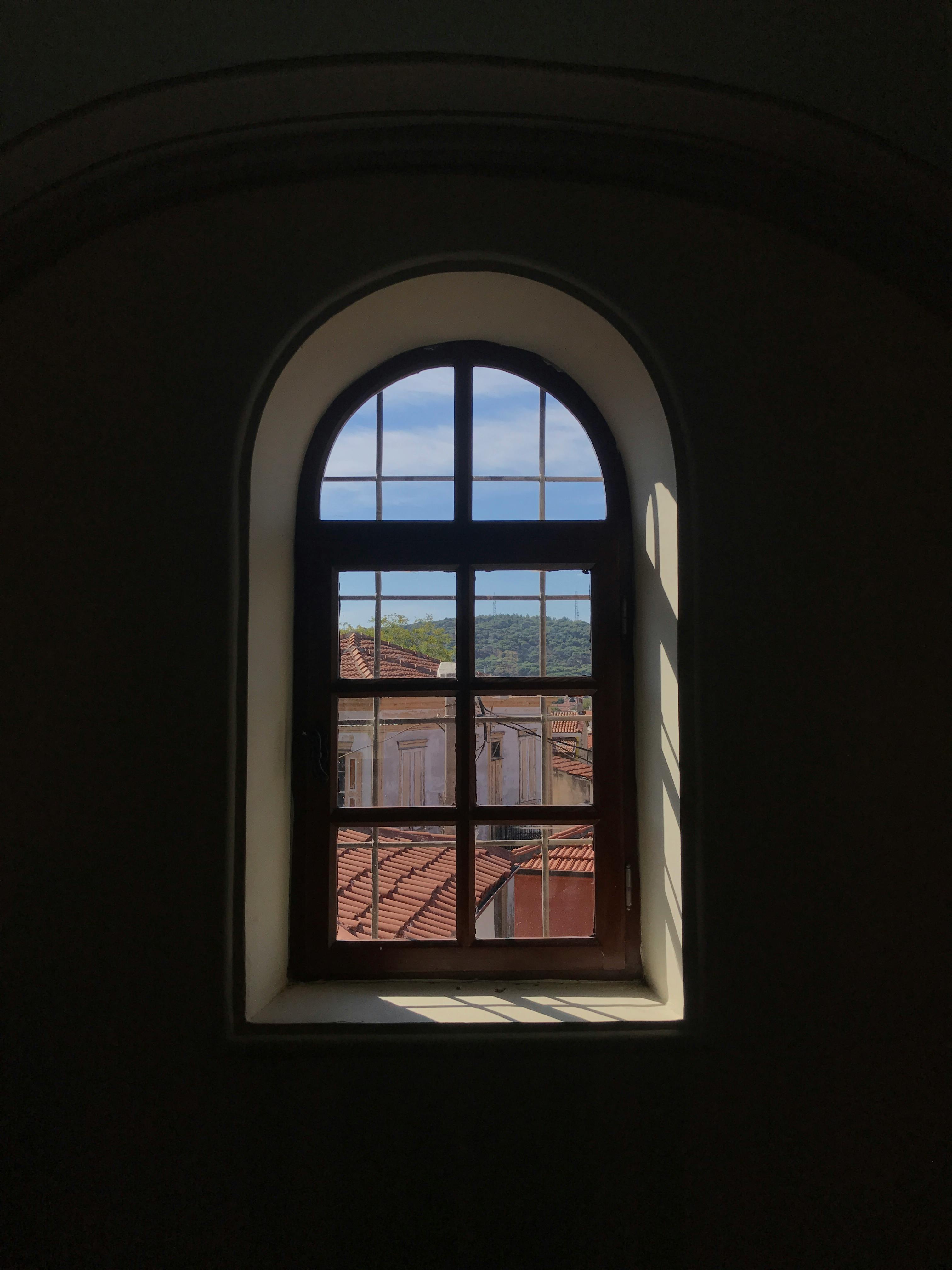 A view from an arched window overlooking rooftops in Ayvalık, Balıkesir, Türkiye. Captures rustic charm.