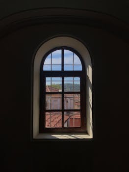 A view from an arched window overlooking rooftops in Ayvalık, Balıkesir, Türkiye. Captures rustic charm.