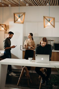 Colleagues relaxing in a modern office break room with laptops and coffee.