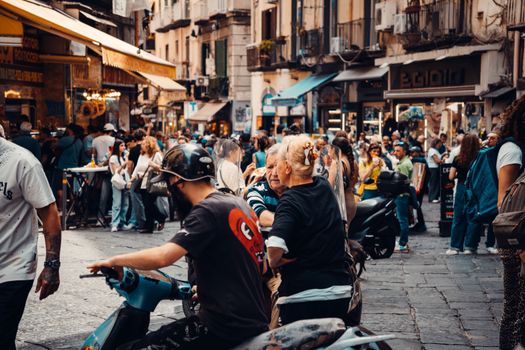 Vibrant European street market bustling with diverse people and scooters in daytime setting.